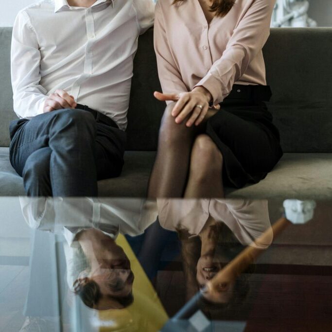 two people sitting next to each other on a couch with their reflection shown on the glass table