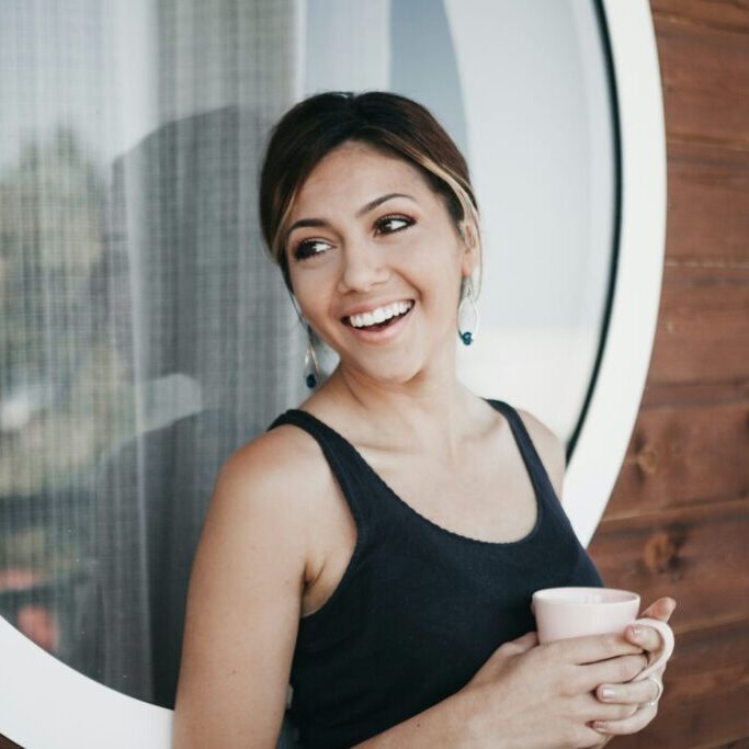 person smiling and holding a mug near window